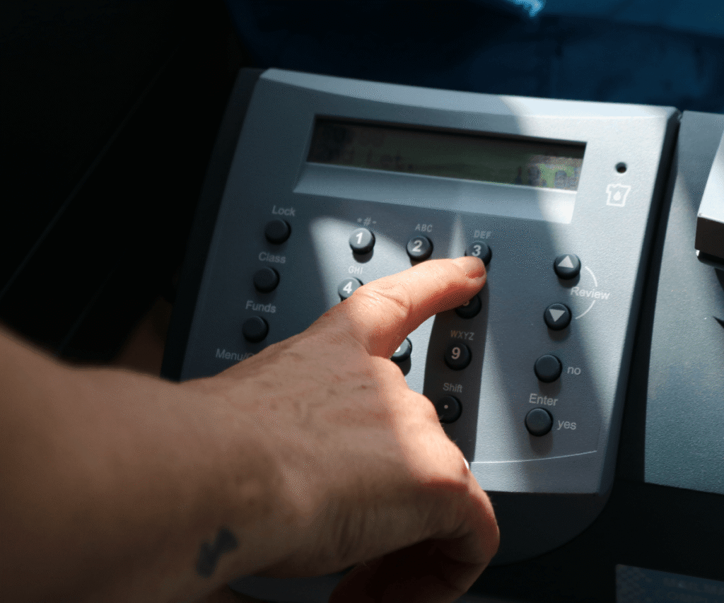 A close-up of a staff member's hand at The Loddon School pressing the number 3 button on the keypad of a grey telephone. A streak of bright sunlight shines across the keypad and the person's hand.