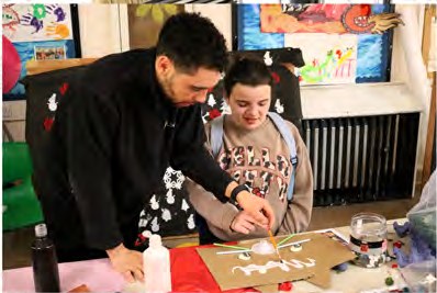 A member of staff supporting a young person with an art activity at a table