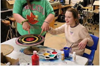 A young person smiling while painting a vinyl record in bright colours