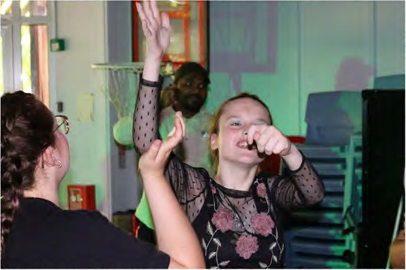 A young person in a black lace dress dancing with her arms in the air under green party lights
